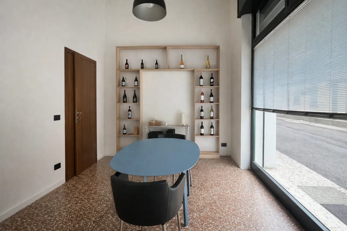 Area caffè coworking Voler.ai Verona — tavolino rotondo con scaffale vini e luce naturale