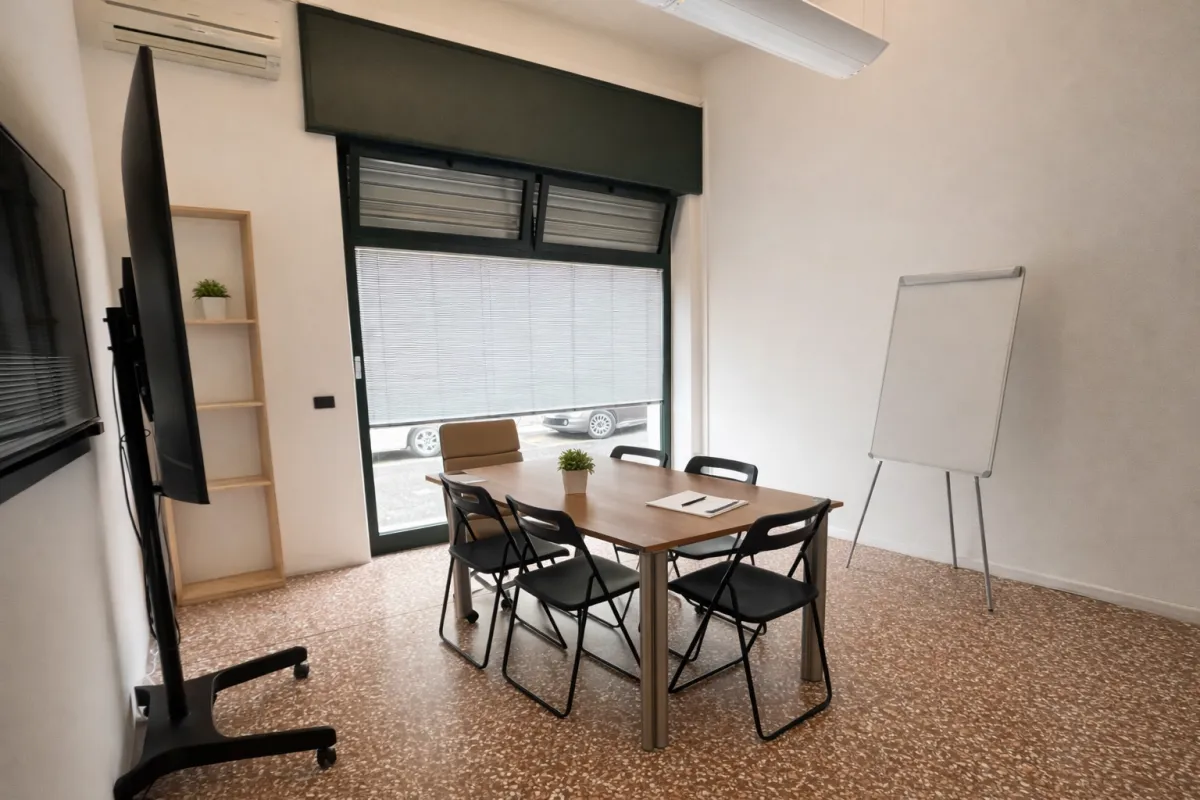 Sala riunioni coworking Voler.ai Verona — tavolo meeting con TV, flipchart e lavagna