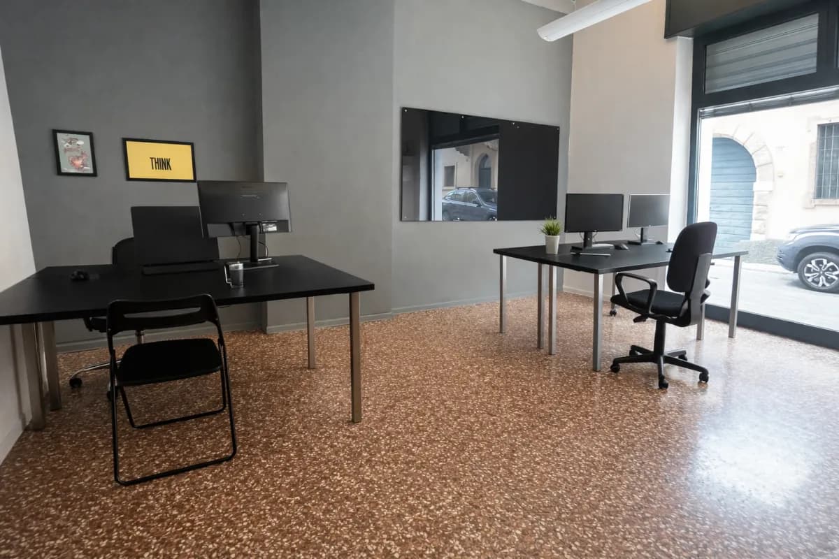 Scrivanie dedicate coworking Voler.ai Verona — open space con monitor, postazioni fisse e luce naturale dal centro storico